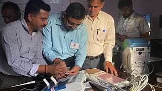 Polling officials check and seal an electronic voting machine before they allow voters to cast their votes at a polling station, India, Saturday, June 1, 2024. 