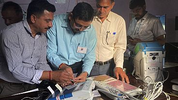 Polling officials check and seal an electronic voting machine before they allow voters to cast their votes at a polling station, India, Saturday, June 1, 2024. 