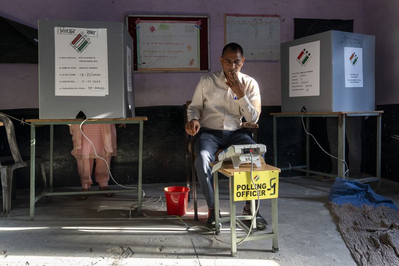 A polling official looks at his device for confirmation as a voter casts her vote in a bye-election in Dharamshala, Saturday, June 1, 2024. 