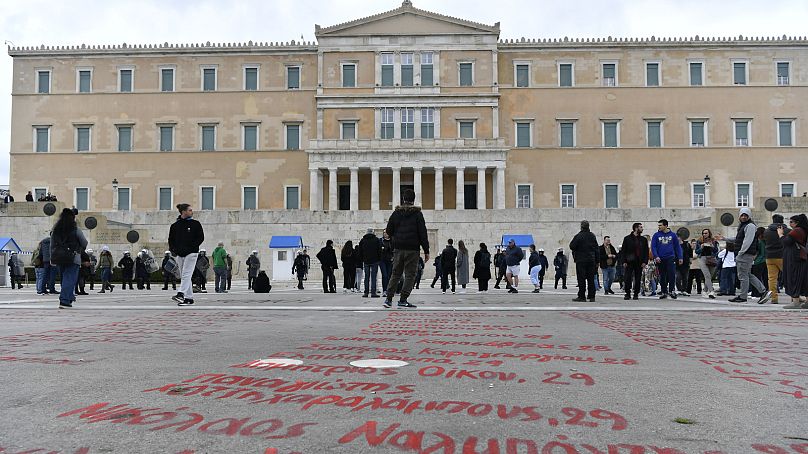 Des personnes passent devant les noms des victimes de la collision ferroviaire de l'année dernière, peints sur un trottoir devant le parlement, à Athènes, Grèce