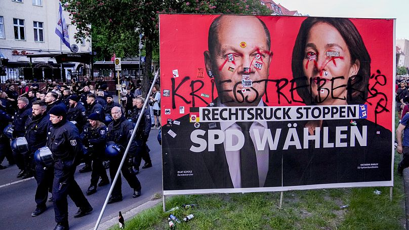 Agentes da polícia passam por um cartaz dos sociais-democratas para as eleições europeias durante a manifestação do Dia do Trabalhador em Berlim