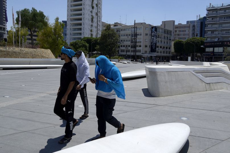 Männer versuchen sich an einem heißen Tag vor der Sonne zu schützen. Sie laufen über den Elephtherias-Platz im Zentrum der Hauptstadt Nikosia, Zypern.