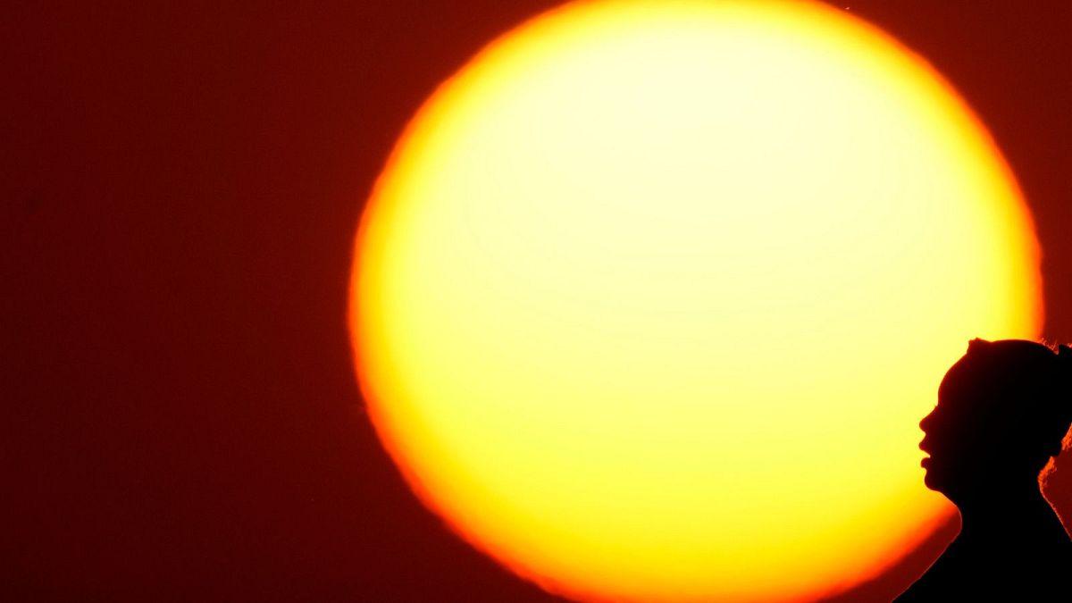 Uma mulher é silhuetada contra o sol poente no meio de índices de calor de três dígitos no Midwest americano, em agosto de 2023.