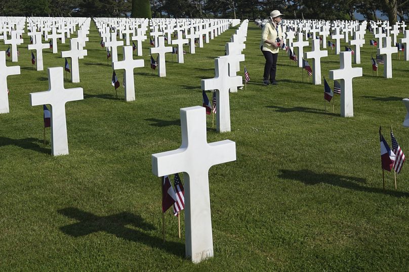 Une femme passe devant des croix et des drapeaux dans un cimetière américain près de Colleville-sur-Mer.