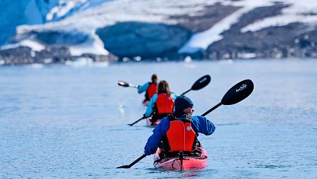 Line of kayakers paddling towards a glacier, Samarinbreen, Svalbard. 
