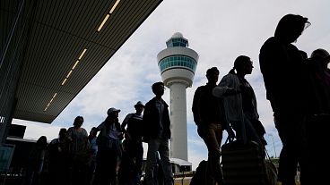 Travelers wait in line outside the terminal building to check in and board flights at Amsterdam's Schiphol Airport.