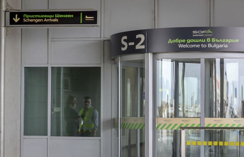 Le personnel de l'aéroport de Sofia se reflète dans une porte indiquant les arrivées Schengen, à l'aéroport de Sofia, Bulgarie.
