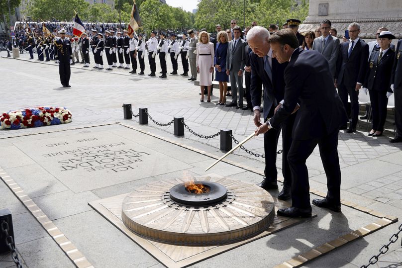 French President Emmanuel Macron, right, and US President Joe Biden rekindle the flame at the Tomb of the Unknown soldier during a ceremony at the Arc de Triomphe, Saturday Ju