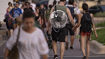 FILE - A girl walks holding hands with a man carrying an electric fan on his back on a hot evening in Bucharest, Romania, July 25, 2023. 