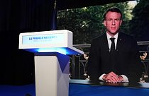 O presidente francês Emmanuel Macron aparece no ecrã de televisão da sede do partido de extrema-direita Rally Nacional na noite das eleições, domingo, 9 de junho de 2024, em Paris