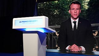 O presidente francês Emmanuel Macron aparece no ecrã de televisão da sede do partido de extrema-direita Rally Nacional na noite das eleições, domingo, 9 de junho de 2024, em Paris