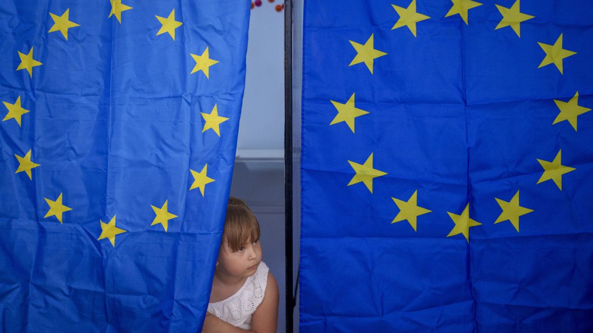 Uma criança espreita de uma cabina de voto durante as eleições europeias e locais em Baleni, Roménia, domingo, 9 de junho de 2024. 