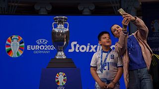 A mother with her boy takes a selfie next to the 2024 UEFA European Football Championship trophy, as it is displayed in Athens, Thursday, March 21, 2024