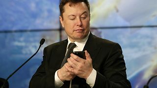Elon Musk pretends to search for an answer to a question on a cell phone during a news conference, January 2020.