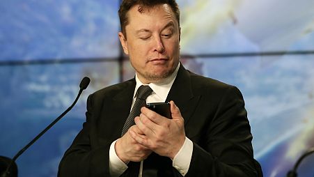 Elon Musk pretends to search for an answer to a question on a cell phone during a news conference, January 2020.