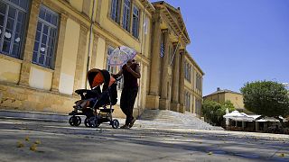  A woman protects herself from the sun with an umbrella as she push a baby in a pushchair during a hot day at Phaneromeni square in central capital Nicosia, 4 June 2024