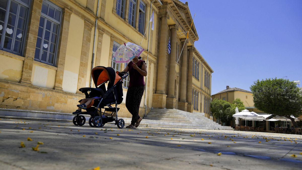 Una donna si protegge dal sole con un ombrello mentre spinge un bambino in un passeggino durante una giornata calda a Nicosia, Cipro, 4 giugno 2024