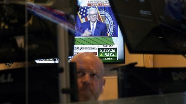 Federal Reserve Chairman Jerome Powell is framed by a trader's screens on the floor of the New York Stock Exchange 