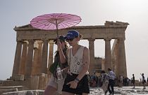 Des touristes avec un parapluie marchent devant le Parthénon sur l'ancienne Acropole dans le centre d'Athènes, mercredi 12 juin 2024. 