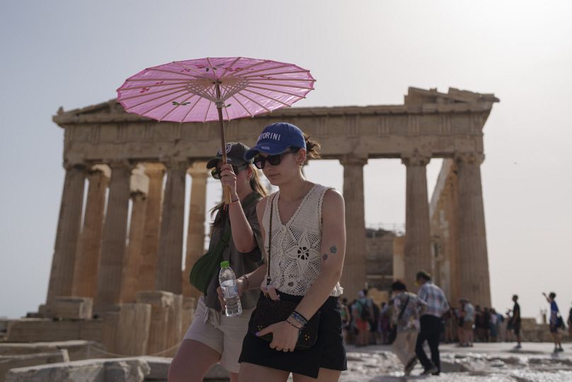 Tourists with an umbrella walk in front of the Parthenon at the ancient Acropolis in central Athens, June 2024