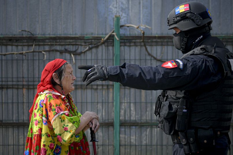 A riot police officer gestures while trying to turn an elderly Romanian Roma woman away during a raid by the National Environmental Guard in Vidra, 13 April 2021