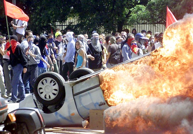 Masked protesters walk past a burning car during clashes between anti-globalisation activists and riot police in Genoa, Italy, 2001.