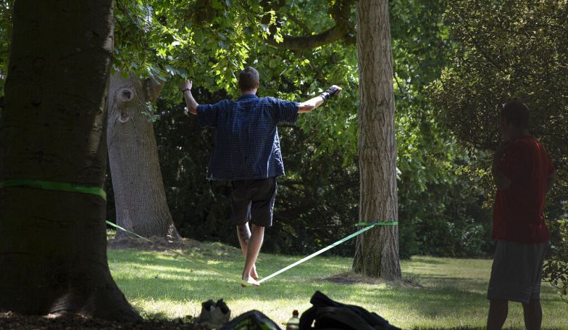 A boy practices his balance on a strap placed between two trees at a park in Ghent, June 2020