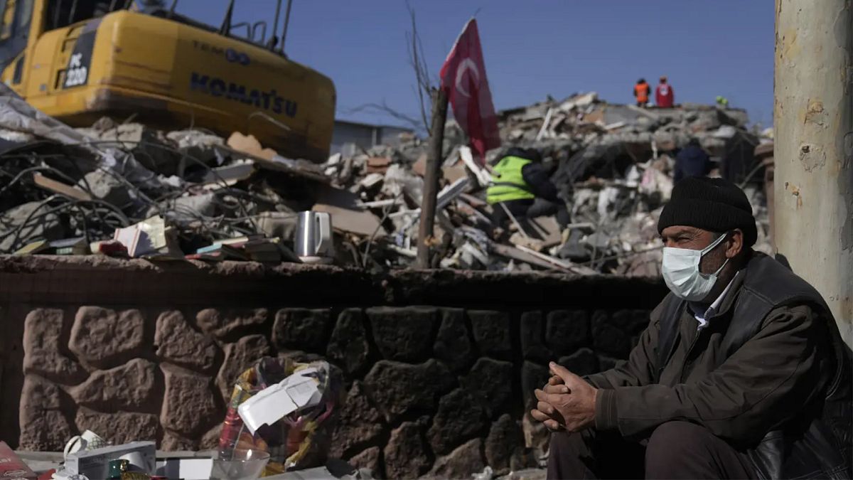 Adıyamanlı bir depremzede, yıkılan bir binanın önünde otururken (12 Şubat 2023)