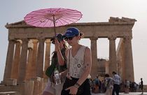 Tourists with an umbrella walk in front of the Parthenon at the ancient Acropolis in central Athens, 12 June 2024. 