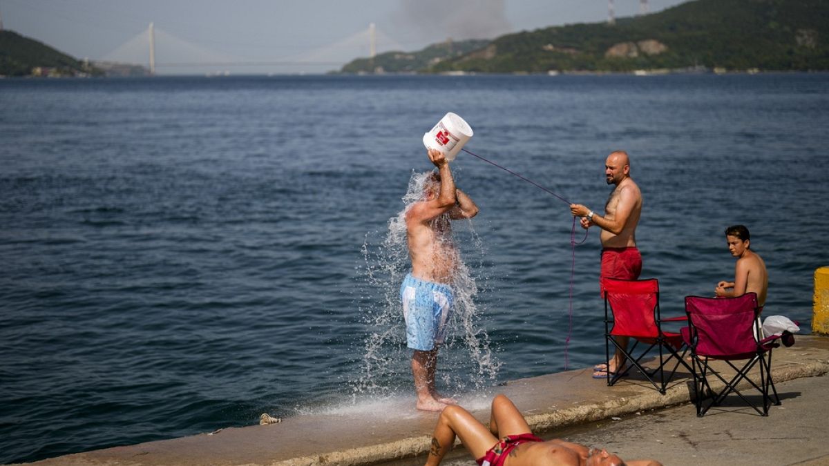 Menschen kühlen sich am Bosporus ab, während im Hintergrund an einem heißen Sommertag in Istanbul Rauch eines Waldbrands aufsteigt, 26. Juli 2023.