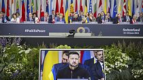 O presidente ucraniano Volodymyr Zelenskyy é visto no ecrã durante a sessão plenária da Cimeira sobre a paz na Ucrânia, em Obbürgen, Suíça, domingo, 16 de junho de 2024
