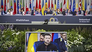 O presidente ucraniano Volodymyr Zelenskyy é visto no ecrã durante a sessão plenária da Cimeira sobre a paz na Ucrânia, em Obbürgen, Suíça, domingo, 16 de junho de 2024