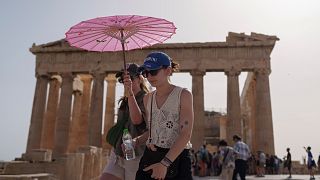 Touristen mit Sonnenschirm vor der Akropolis im Zentrum Athens, Mittwoch, 12. Juni 2024. 