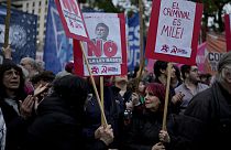 A woman holds a banner, right, that reads in Spanish, "The criminal is Milei"during a demonstration at the Plaza de Mayo demanding the release of those detained in a protest.