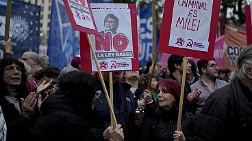 A woman holds a banner, right, that reads in Spanish, "The criminal is Milei"during a demonstration at the Plaza de Mayo demanding the release of those detained in a protest.