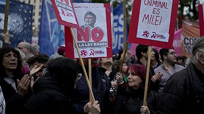 A woman holds a banner, right, that reads in Spanish, 