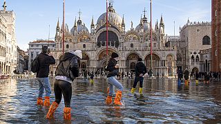 Varias personas cruzan la Plaza de San Marcos, inundada por la marea, en Venecia, Italia, el sábado 4 de diciembre de 2021. El agua alcanzó los 99 centímetros sobre el nivel del mar y las partes más bajas de la ciudad se wen