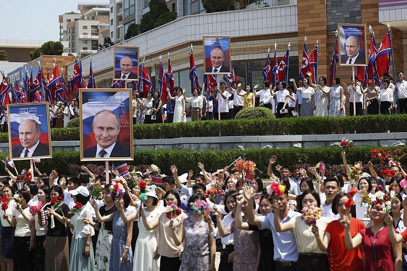 Rusya Devlet Başkanı Vladimir Putin'in portrelerini tutan insanlar, resmi konvoyu alkışlıyor, Pyongyang, Kuzey Kore, 19 Haziran 2024.