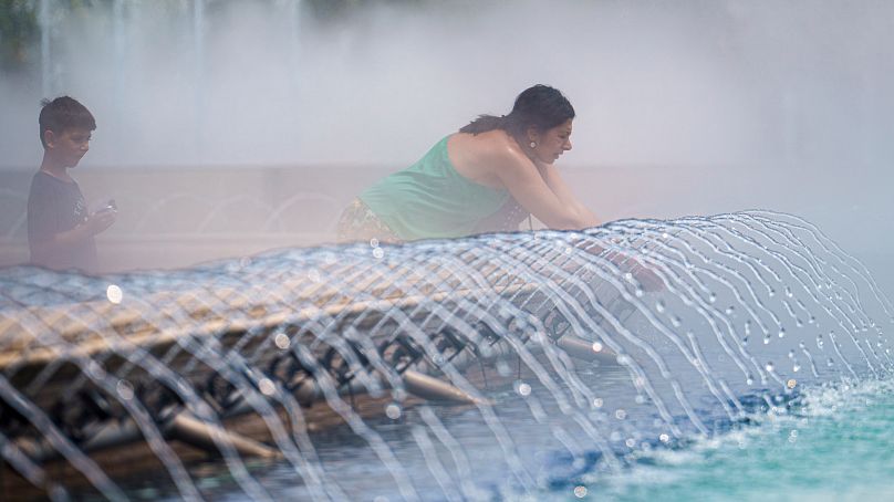 A woman cools off next to a public fountain in Bucharest, Romania, Wednesday, June 19, 2024 as temperatures reach 36 degrees.