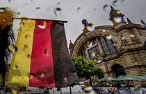 Μια μικρή γερμανική εθνική σημαία κυματίζει μπροστά από τον κεντρικό σιδηροδρομικό σταθμό της Φρανκφούρτης, Γερμανία, μια βροχερή Τετάρτη, 19 Ιουνίου 2024. (AP Photo/Michael Probst)