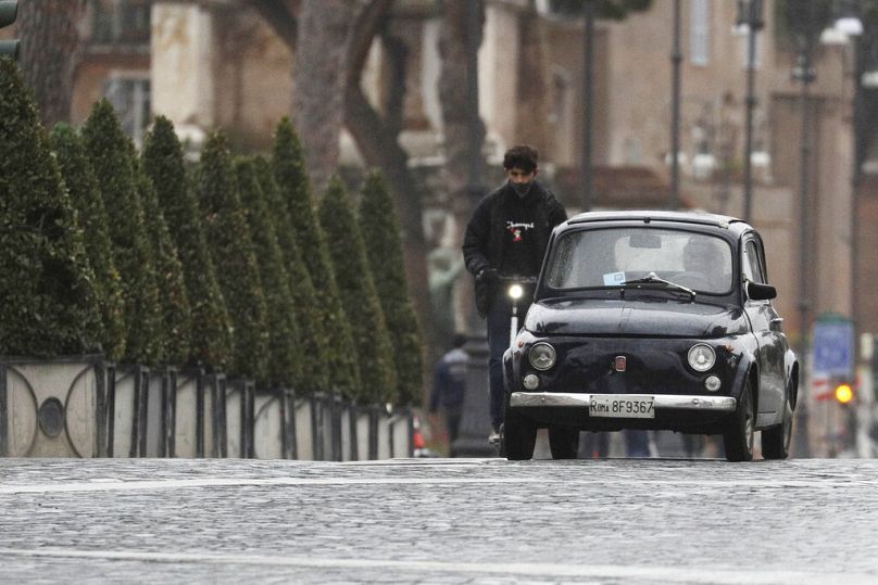 An old FIAT 500 car is followed by a man riding his electric scooter in Rome, 22 January 2021