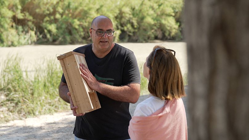 Neftalí Escribano muestra a Andrea Bolitho, de Euronews, una de las cajas de madera para murciélagos que se colgarán en los árboles junto al río.
