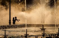 Des enfants profitent de la bruine d'une fontaine publique avant le coucher du soleil à Bucarest, Roumanie, jeudi 20 juin 2024.