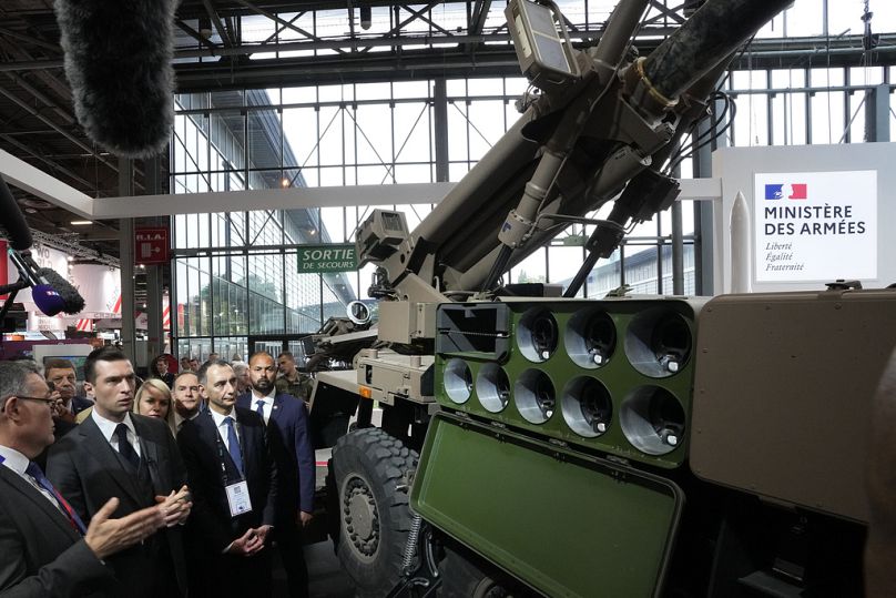 Jordan Bardella, second left, president of the far-right National Front party, looks at a Caesar self-propelled howitzer at the Eurosatory Defense and Security exhibition