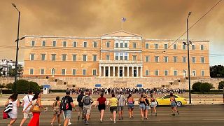 Smoke from wildfires is seen above the Greek parliament building in central Athens, 11 August, after a blaze northeast of the capital forced evacuations in the area.