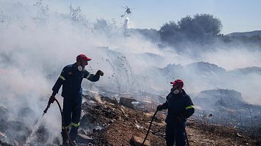 I vigili del fuoco cercano di spegnere l'incendio mentre un elicottero getta acqua nel sobborgo di Koropi, nella parte orientale di Atene, il 19 giugno 2024.