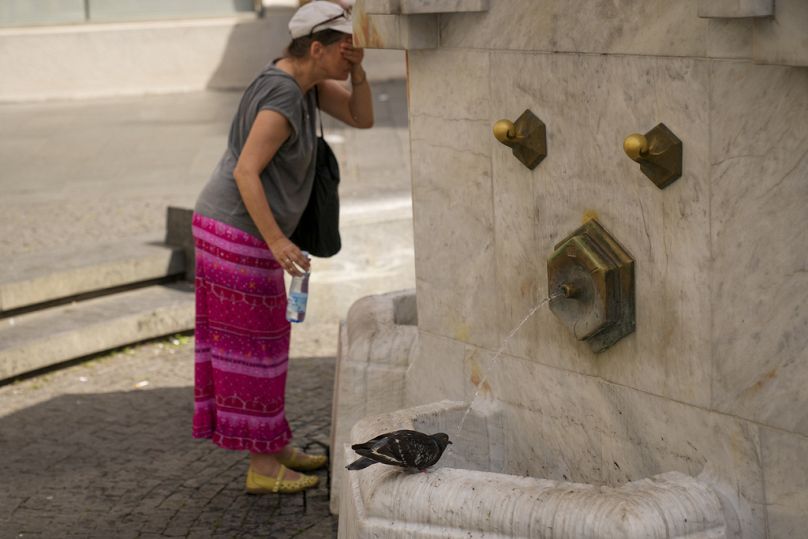 A woman cools herself as a pigeon drinks water from a public fountain in Belgrade, Serbia.