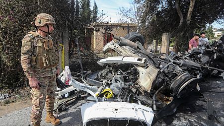 ضابط في الجيش اللبناني يقف بجوار سيارة استهدفتها غارة إسرائيلية في الضواحي الجنوبية لمدينة صور، لبنان، الأربعاء 13 مارس 2024.