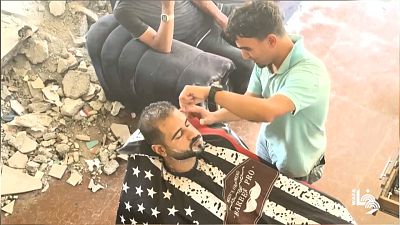 الحلاق عبدالله توفيق رمضان يحلق لزبون في صالونه شبه المدمر في مخيم البريج بقطاع غزة