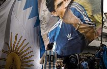 امرأة تلوح بلافتة عليها صورة أسطورة كرة القدم دييغو مارادونا